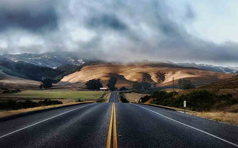 Long open road leading into rolling hills under low clouds